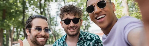 Позитивні багатоетнічні друзі в сонцезахисних окулярах проводять час у літньому парку, банер — стокове фото
