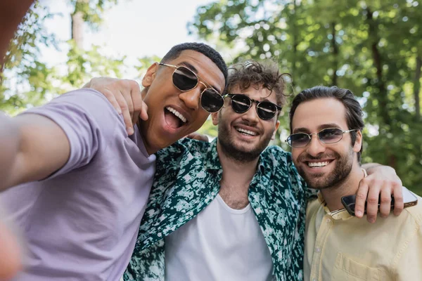 Excited interracial friends in sunglasses hugging in summer park — Stock Photo