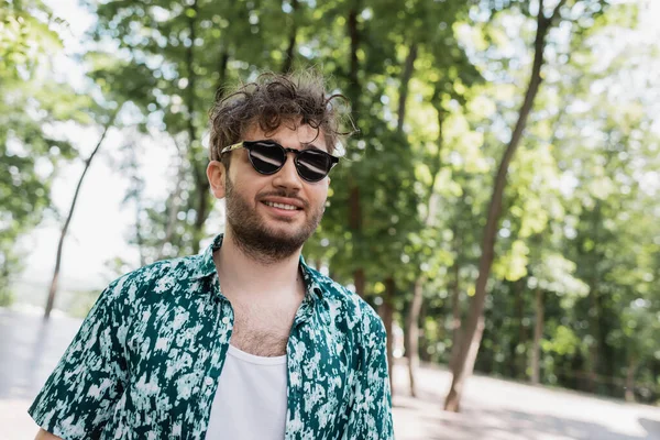 Улыбающийся мужчина в повседневной одежде и солнечных очках в летнем парке — стоковое фото
