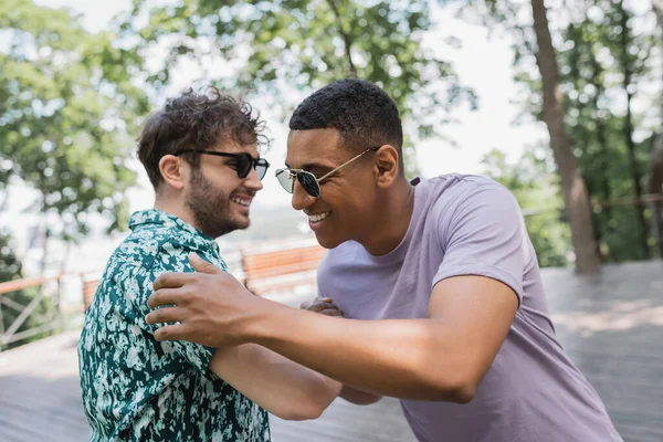 Amigos multiétnicos positivos en la reunión de gafas de sol en el parque de verano - foto de stock