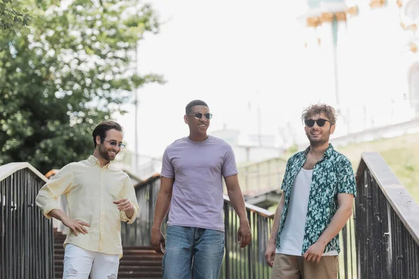 Des hommes interraciaux positifs avec des lunettes de soleil marchant dans les escaliers du parc d'été — Photo de stock