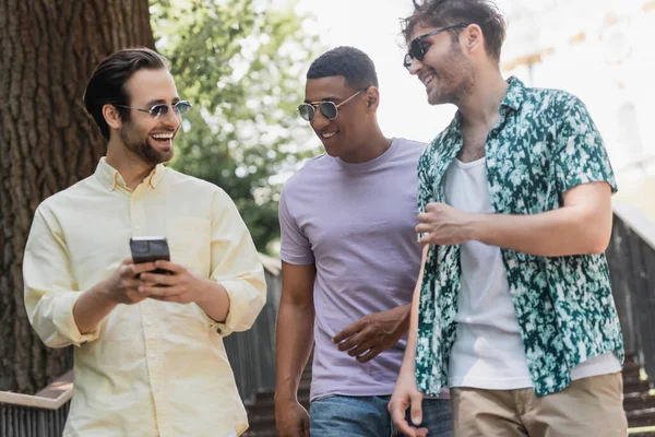 Positive multiethnic friends using smartphone while walking on stairs in park in summer — Stock Photo