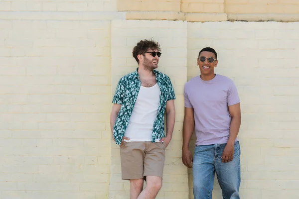 Positive interracial friends in sunglasses standing near building in Kyiv — Stock Photo
