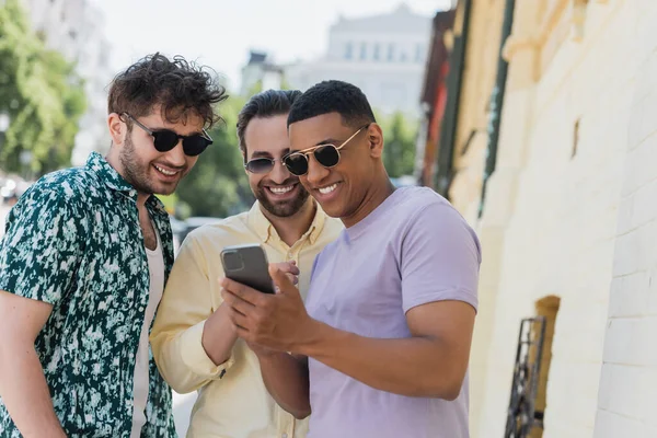Hombres multiétnicos en gafas de sol con smartphone en la calle urbana de Kiev - foto de stock