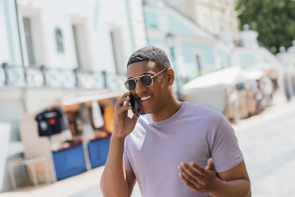 Overjoyed african american man in sunglasses talking on mobile phone on urban street — Stock Photo