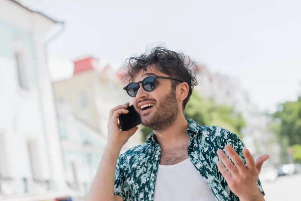 Excited man in sunglasses talking on smartphone on urban street — Stock Photo