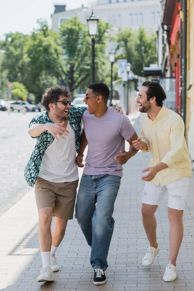 Cheerful man hugging african american friend while walking on Andrews descent in Kyiv — Stock Photo