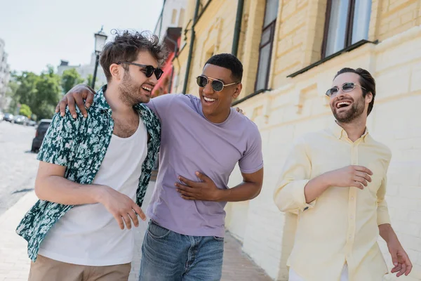 Позитивні міжрасові чоловіки в сонцезахисних окулярах йдуть по Андріївському спуску в Києві. — стокове фото