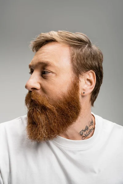 Портрет татуированного мужчины в футболке, смотрящего в сторону изолированного на сером — стоковое фото
