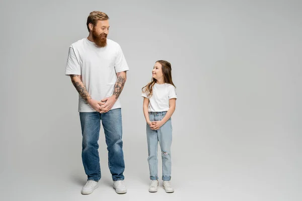 Повна довжина позитивного батька і дочки, дивлячись один на одного на сірому фоні — стокове фото