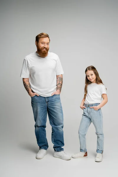 Tattooed man and preteen daughter posing with hands in pockets on grey background — Stock Photo