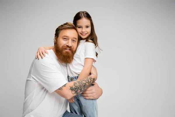 Lächelnd tätowierter Vater umarmt glückliche Tochter isoliert auf grau — Stockfoto