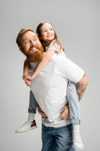 Sonriente padre sosteniendo hija preadolescente y mirando hacia otro lado aislado en gris - foto de stock