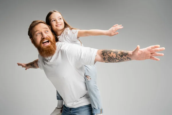 Беззаботная девушка, сидящая на татуированном отце и веселящаяся вместе, изолированная от серых — стоковое фото