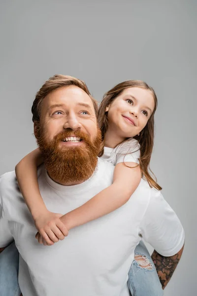 Улыбающаяся девушка, которая сидит на бородатом родителе и смотрит в сторону, изолированную от серых — стоковое фото