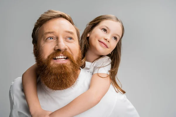 Preteen gamin regarder loin tout en piggyback sur sourire barbu papa isolé sur gris — Photo de stock