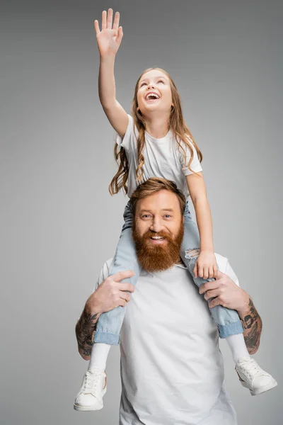 Cheerful kid raising hand while sitting on shoulders of father isolated on grey — Stock Photo
