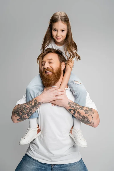 Smiling girl sitting on shoulders of tattooed dad isolated on grey — Stock Photo