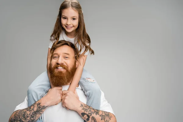 Hombre alegre sosteniendo hija preadolescente sobre hombros aislados en gris - foto de stock