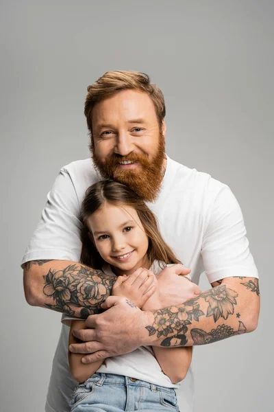 Позитивный татуированный родитель обнимает дочь-подростка, изолированную от серых — стоковое фото