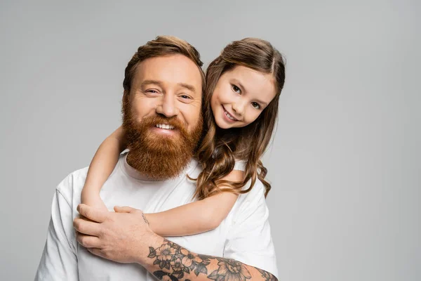 Fille positive étreignant le père tatoué en t-shirt isolé sur gris — Photo de stock