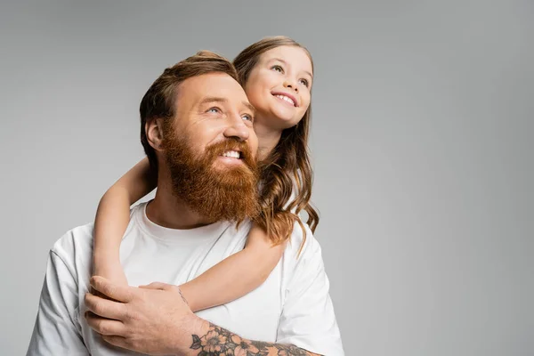 Chica positiva abrazando padre y mirando hacia otro lado aislado en gris - foto de stock