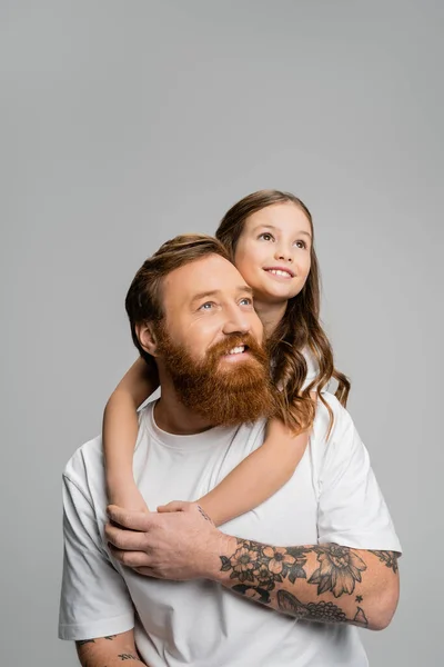 Positive girl hugging tattooed father and looking away isolated on grey — Stock Photo