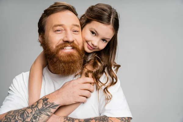 Preteen menina abraçando positivo e tatuado pai isolado no cinza — Fotografia de Stock
