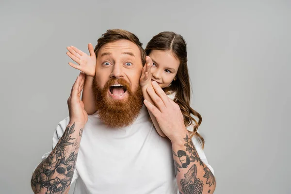 Lächelndes Mädchen berührt Gesicht des aufgeregten Vaters isoliert auf grau — Stockfoto