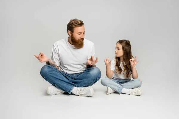 Kid and bearded dad doing gyan mudra while sitting on grey background — Stock Photo