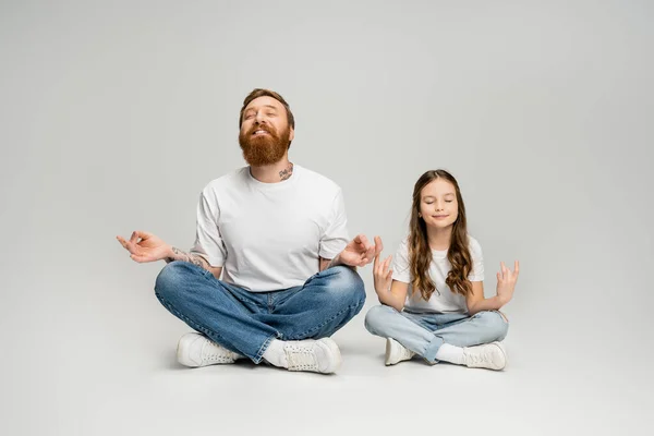 Улыбающиеся мужчина и дочь, занимающиеся гьянской мудрой, медитируя на сером фоне — стоковое фото