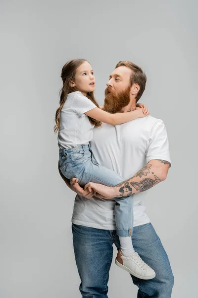 Татуированный мужчина держит в руках дочь-подростка и разговаривает изолированно на серой — стоковое фото