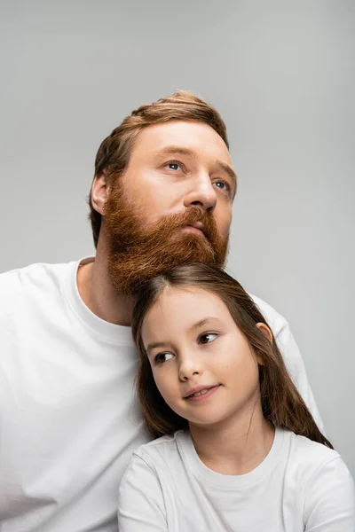 Retrato de hombre e hija barbudos en camisetas blancas mirando hacia otro lado aislados en gris - foto de stock