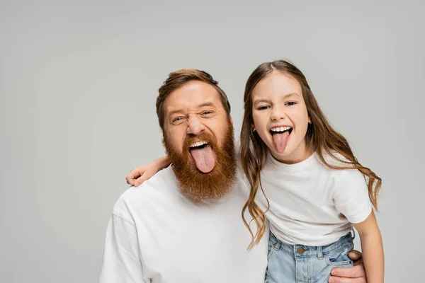 Padre e hija en camisetas blancas sobresaliendo lenguas aisladas en gris - foto de stock