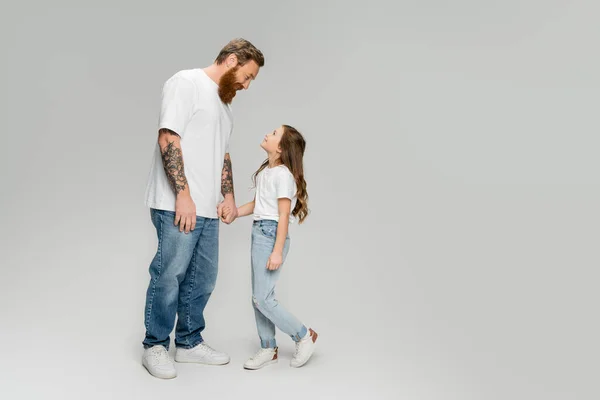 Side view of smiling dad and daughter holding hands on grey background — Stock Photo