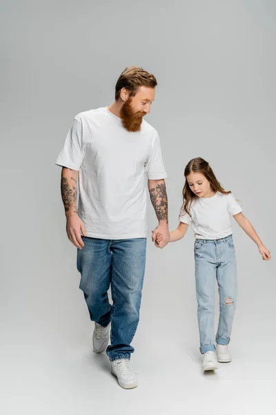 Татуйований чоловік тримає руку дочки під час ходьби на сірому фоні — стокове фото
