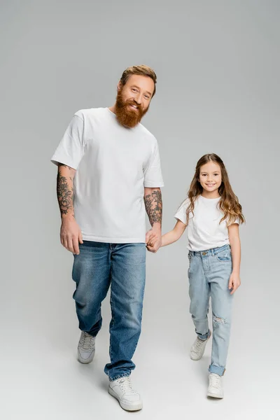 Full length of smiling man and daughter holding hands while walking on grey background — Stock Photo