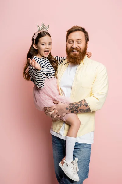 Веселый бородатый мужчина держит дочь-подростка в бандаже на розовом фоне — стоковое фото