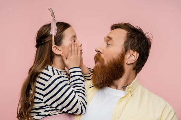 Seitenansicht eines bärtigen Mannes, der seine Tochter mit einem Stirnband ansieht, das Wangen berührt, isoliert auf rosa — Stockfoto