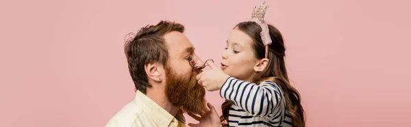 Child with crown headband curling eyelashes of father isolated on pink, banner — Stock Photo