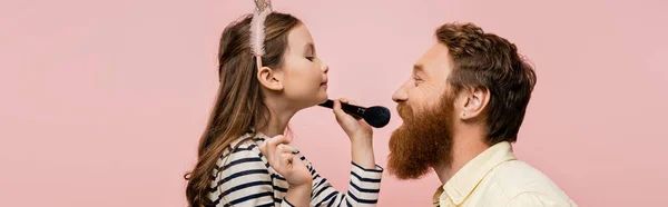 Preteen kid in headband holding make-up brush near bärtiger dad isolated on pink, banner — Stockfoto