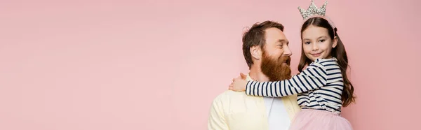 Lächelnder bärtiger Mann mit Kronenstirnband auf rosafarbenem Banner und Blick auf frühgeborene Tochter — Stockfoto