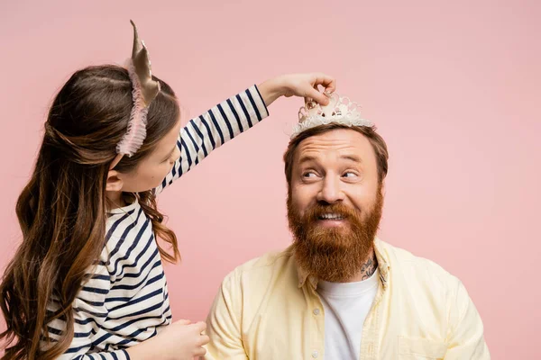 Preteen Mädchen mit Stirnband trägt Krone auf lächelndem Vater isoliert auf rosa — Stockfoto
