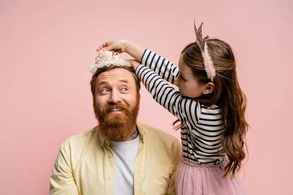 Preteen daughter wearing crown headband on bearded dad isolated on pink — Stock Photo