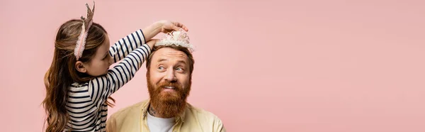 Child wearing crown headband on smiling bearded dad isolated on pink, banner — Stock Photo