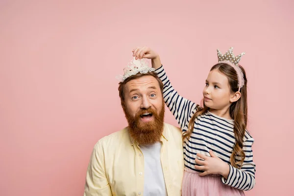 Preteen girl wearing crown headband on excited dad isolated on pink — Stockfoto