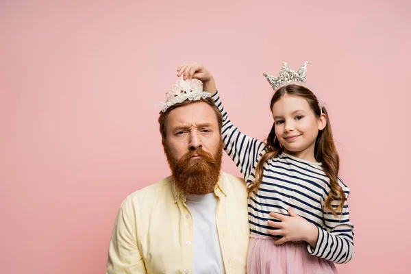 Lächelndes Mädchen mit Krone auf ernstem Papa isoliert auf rosa — Stockfoto