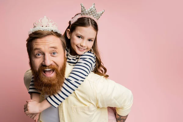 Sonriente niña abrazando padre con diadema de corona aislado en rosa — Stock Photo