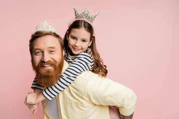 Sorgenfreies Mädchen huckepack auf bärtigen Papa mit Krone Stirnband isoliert auf rosa — Stockfoto