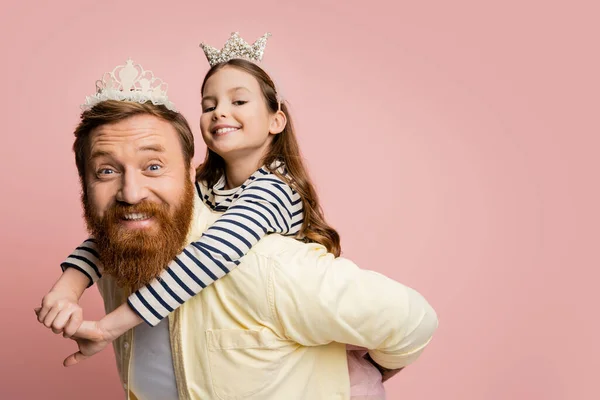 Criança alegre piggybacking no pai com a cabeça da coroa isolado em rosa — Fotografia de Stock
